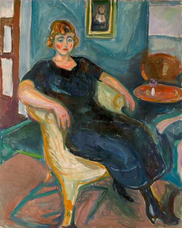 Frau in dunklem Kleid sitzt im gelben Korbsessel vor blauer Wand mit Bild – Edvard Munch Modell im Korbsessel Kunstkopie