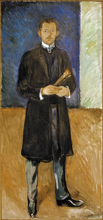 Stehender Mann im dunklen Mantel mit Pinseln in der Hand vor heller Wand – Edvard Munch Selbstbildnis mit Pinseln Kunstkopie