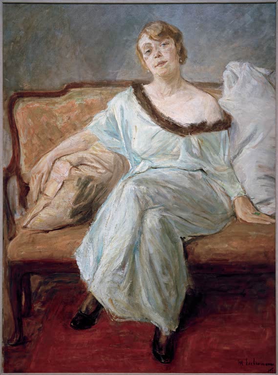 Frau in hellblauem Kleid mit Pelzbesatz lehnt auf einem Sofa mit Kissen – Max Liebermann Lola Leder Kunstkopie
